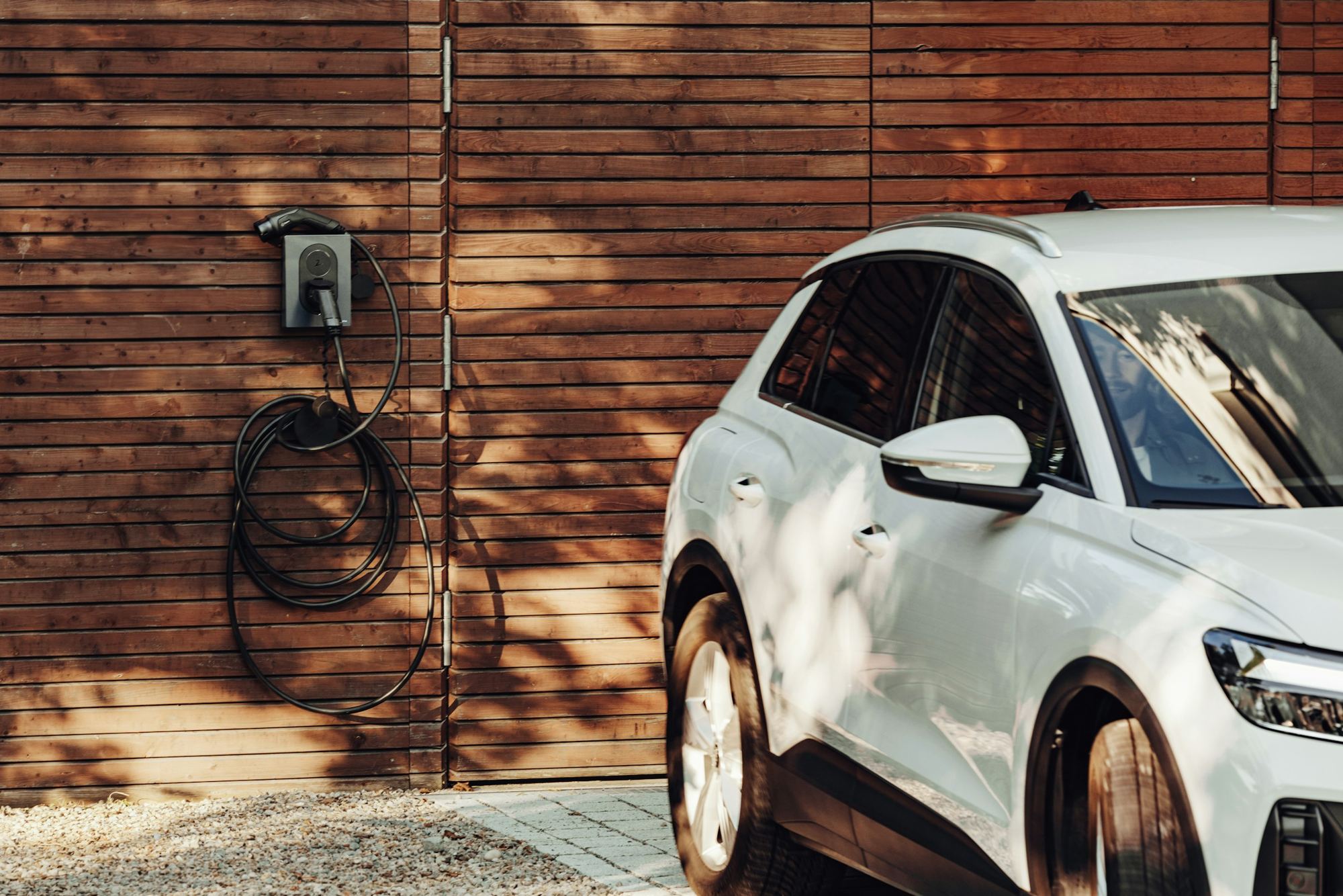 A home EV charger mounted on a wall beside a parked white car